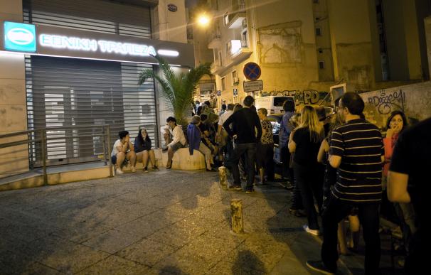 Varios ciudadanos griegos hacen cola delante de un cajero por la noche
