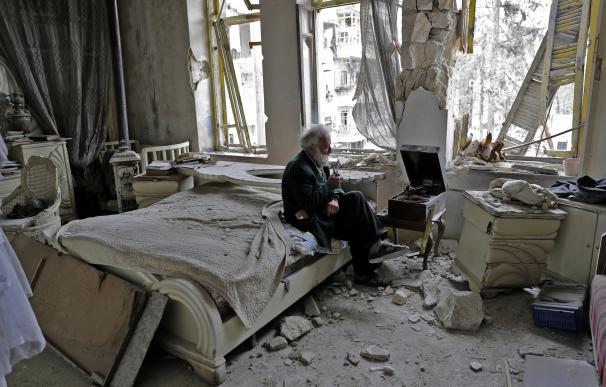 Mohammad Mohiedine Anis, de 70 años, fuma su pipa mientras escucha música en su gramófono en su destrozada casa de Alepo (JOSEPH EID / AFP)
