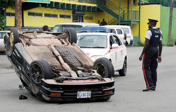 Un policía observa un auto destrozado en una calle de unos de los barrios del centro en Kingston (Jamaica).