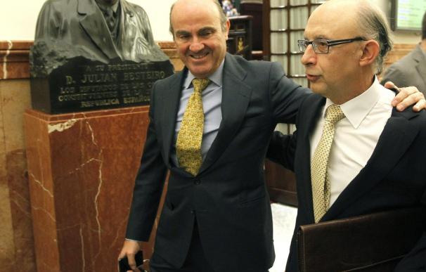 El ministro de Economía, Luis de Guindos (i) y el titular de Hacienda, Cristóbal Montoro, se saludan en los pasillos del Congreso de los Diputados.