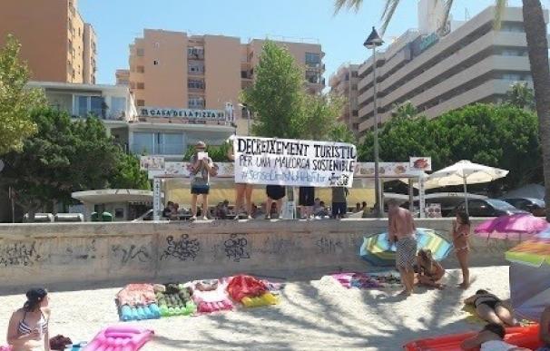 Jóvenes del GOB despliegan una pancarta en la playa de S'Arenal por el "decrecimiento turístico"