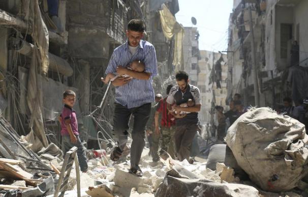 Dos hombres sirios mientras rescatan a dos bebés de una zona destruída tras un bombardeo en Alepo