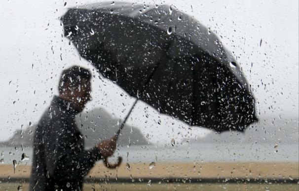 Un hombre se protege de la lluvia con una paraguas mientras pasea junto a la bahía de La Concha de San Sebastián. (Juan Herrero / EFE)