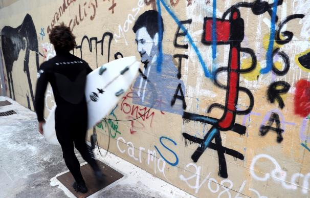 Un surfista pasa junto a una pintada a favor de la banda terrorista ETA en el barrio de Gros de San Sebastian. EFE/Juan Herrero