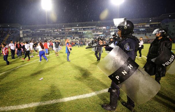Aficionados ingresan al campo y se protegen de los gases lacrimógenos lanzados por las autoridades, debido a los disturbios a las afueras del Estadio Nacional por la cancelación del clásico entre Olimpia y Motagua hoy sábado, en Tegucigalpa. Al menos tres