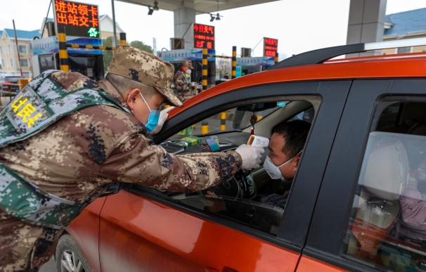 Un militar chino toma la temperatura a un ciudadano en una carretera a las afueras de Wuhan. / EFE