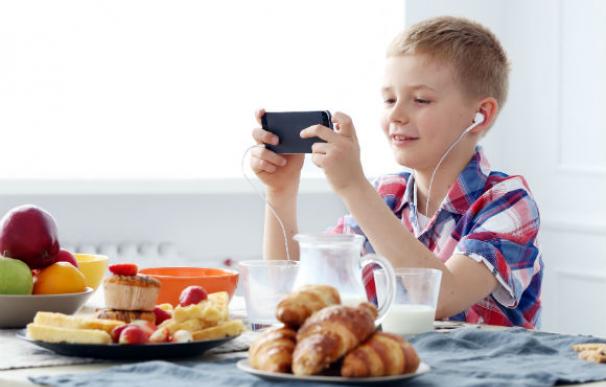 Un niño desayuna mientras juega con un móvil