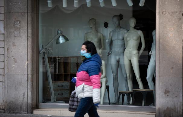 Una mujer protegida con una mascarilla pasa junto a un escaparate de una tienda cerrada durante el noveno día laborable desde que se decretó el estado de alarma en el país a consecuencia del coronavirus, en Barcelona/Catalunya (España) .