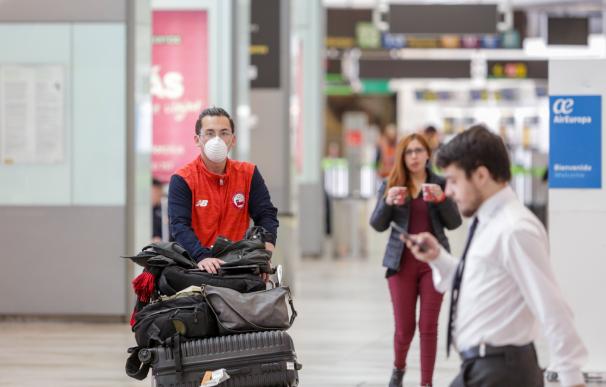 Un operario con mascarilla traslada maletas en el aeropuerto de Barajas, casi vacío