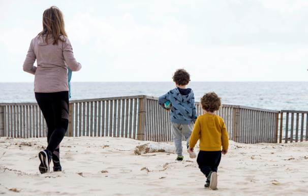 Dos niños acompañados por su madre en una playa de Menorca