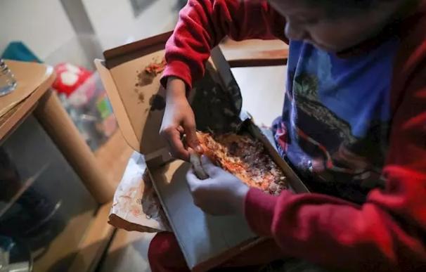 Un niño come un trozo de pizza del menú infantil de Telepizza mientras ve la televisión en su casa. /Jesús Hellín/ Europa Press