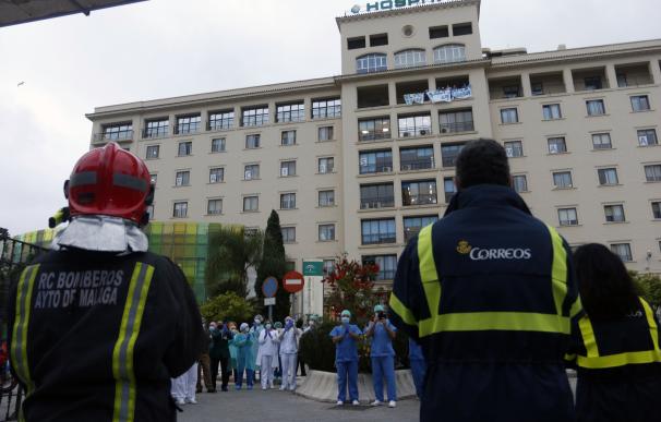 Bomberos realizan junto a trabajadores de Correos el aplauso a los sanitarios, en la puerta principal del Hospital Regional de Málaga.