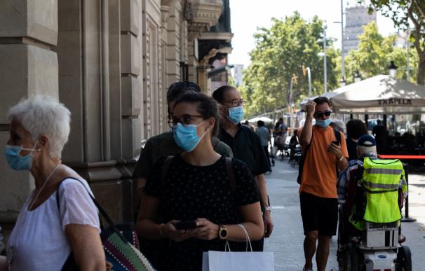 Decenas de personas protegidas con mascarilla hacen cola para entrar en una biblioteca, en Barcelona
