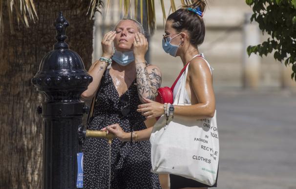 Dos turistas internacionales se refrescan en una fuente de Sevilla durante el mes de agosto.