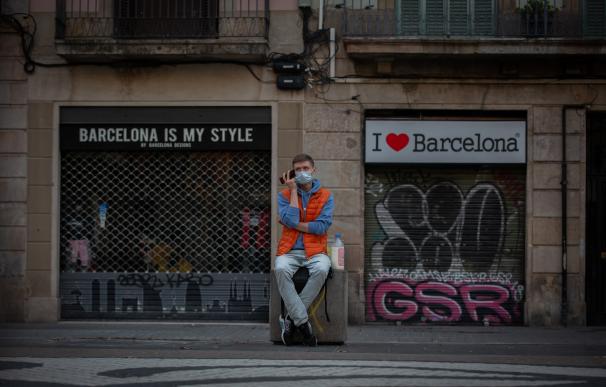 Un hombre se sienta delante de varios comercios turísticos cerrados en Barcelona.