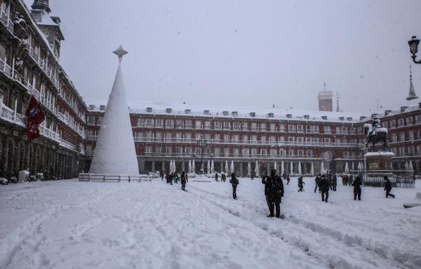 Varias personas caminan bajo la nieve en la Plaza Mayor de Madrid
