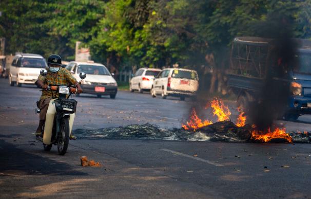 Un hombre en motocicleta atraviesa una barricada de fuego en Myanmar.
