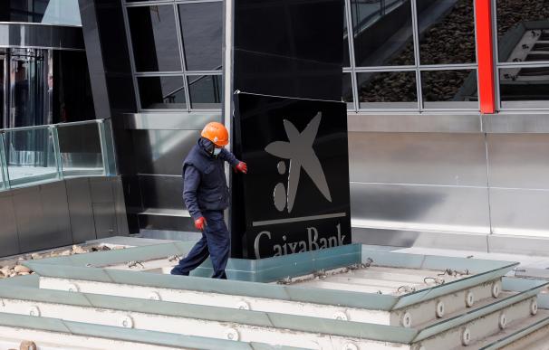Operarios sustituyen este sábado uno de los rótulos de Bankia por otro de la nueva CaixaBank en las torres Kio de Madrid, sede operativa del banco nacionalizado estos últimos años.
