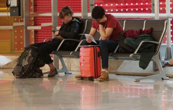 Dos personas con su equipaje esperan su vuelo sentados en un banco en el Aeropuerto de Madrid-Barajas Adolfo Suárez.