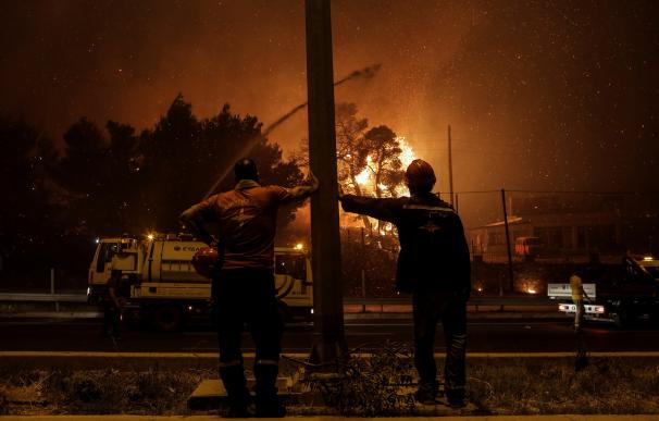 Bomberos voluntarios miran las llamas acercándose a una autopista en la zona de Afidnes, en Atenas (Grecia).