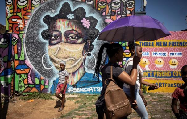 Los residentes de Soweto caminan frente a una obra de arte de graffiti en mitad del caos por la nueva cepa.