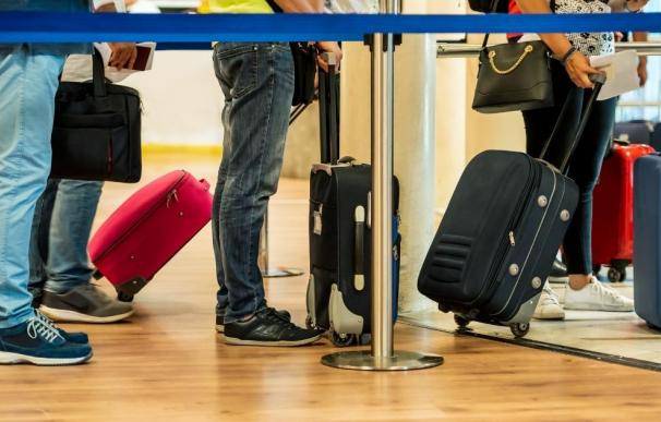 Personas haciendo cola en el aeropuerto con sus maletas