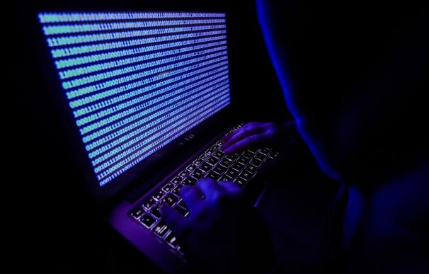 A person dressed as an internet hacker is seen with binary code displayed on a laptop screen in this illustration photo taken in Krakow, Poland on August 17, 2021. (Photo by Jakub Porzycki/NurPhoto via Getty Images)