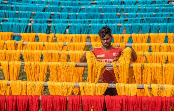 Un trabajador cuelga hilos de algodón de colores recién teñidos