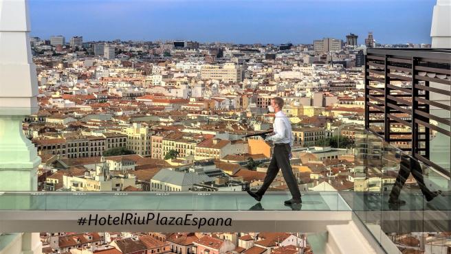 Untrabajador con mascarilla cruza la pasarela del Hotel Riu Plaza España